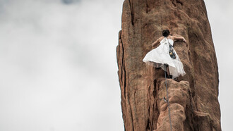 In her white wedding dress, the woman embodies the essence of feminine consciousness as she climbs the brown rock under the pure white sky, symbolizing her innate strength, determination, and the sacred union of her inner and outer worlds