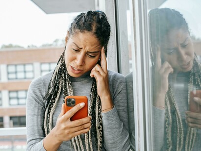 A tired Black woman uses her smartphone on the street, her expression conveying concern