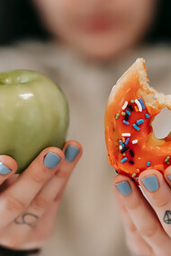 Woman holding an apple in one hand and a donut in the other emphasizes the importance of a preventive diet against cancer