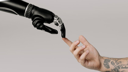 A human hand and a sleek black robot hand draw near to one another, symbolizing the convergence of human ingenuity and artificial intelligence