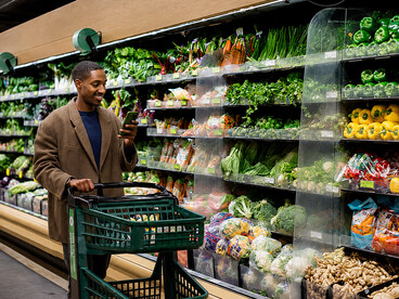 Customer selecting fresh fruits and vegetables in a supermarket aisle, highlighting modern shopping habits and food choices