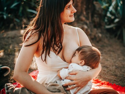A mother gently nursing her infant in a natural setting, reflecting the intimate connection between breastfeeding and early development