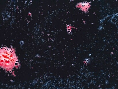 Soft pink foam bubbles floating on dark, reflective water