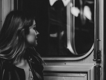 Side view of a woman wearing a black jacket, sitting alone on a subway and looking outside